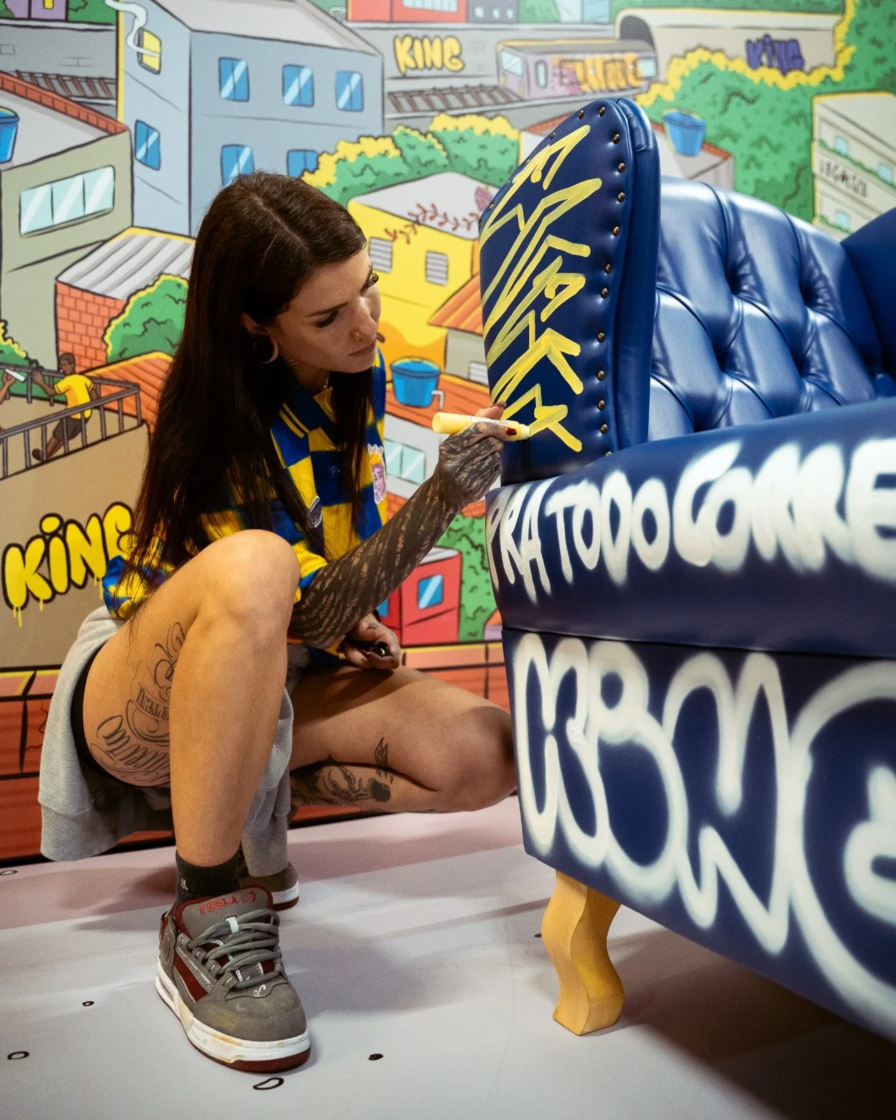 Artista pintando o trono azul com spray, com a assinatura Pra Todo Corre