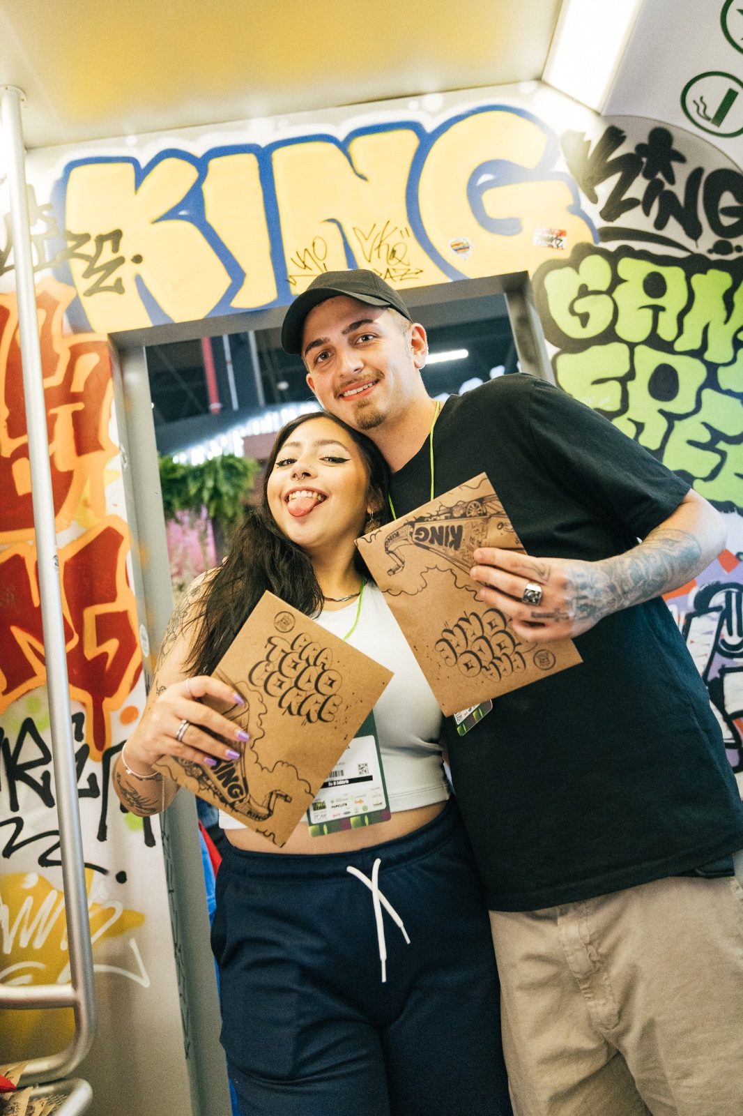 Casal com sacolas da KING em frente ao grafite do estande