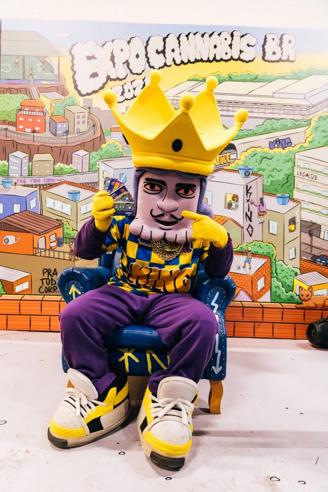 Mascote KINGÃO sentado no trono em frente ao painel ilustrado