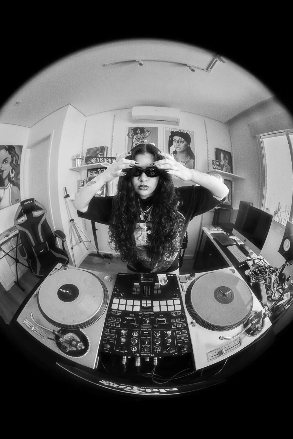 DJ Sophia entre os toca-discos em fotografia preto e branco