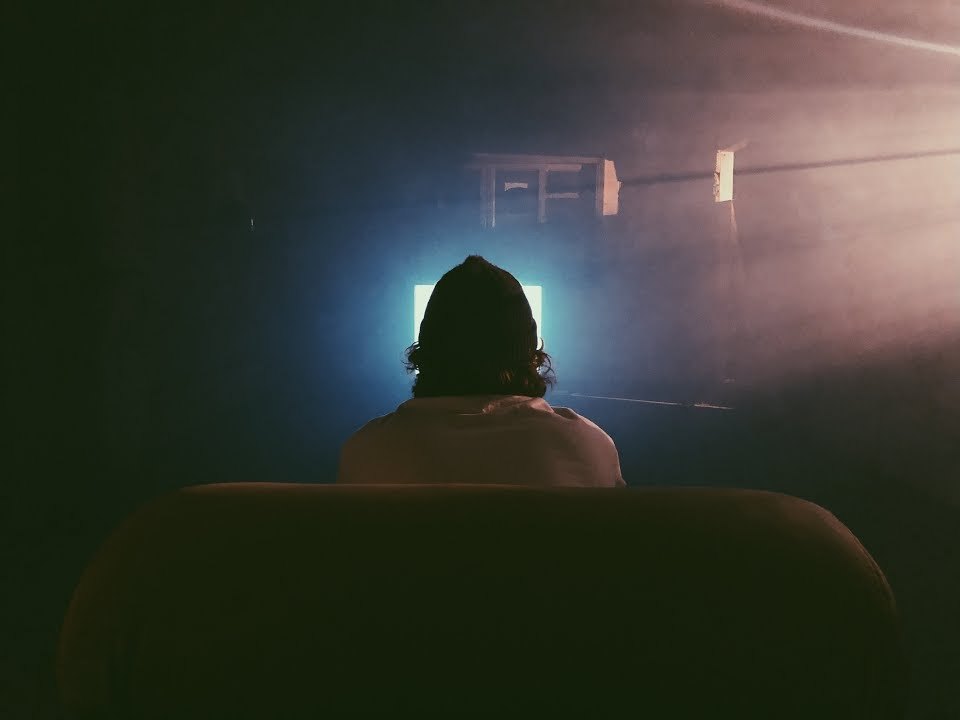 Frame do clipe Chega de Falar de Ice: figura sozinha de costas diante de uma tela azul, na fumaça.