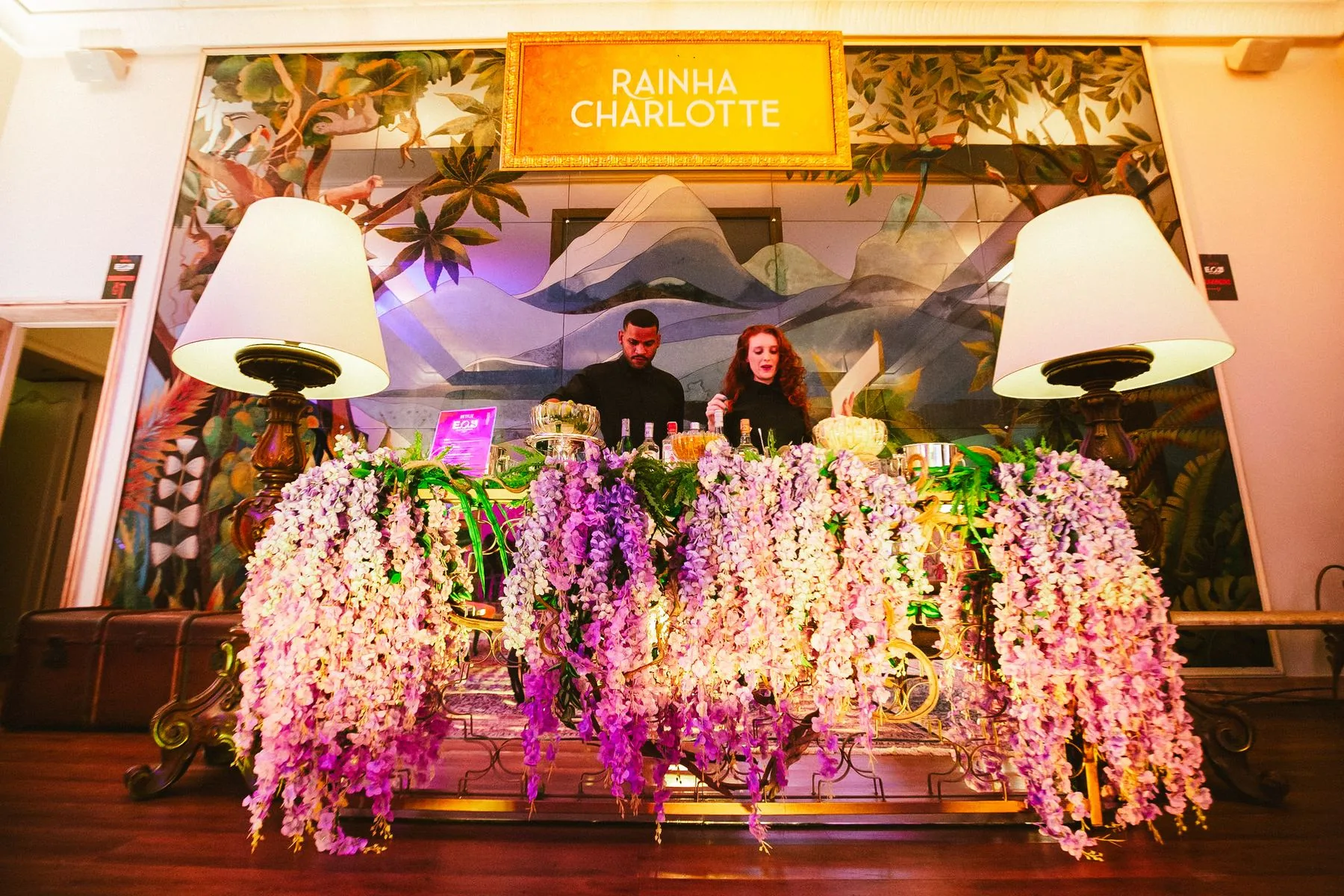 Bar da Rainha Charlotte com cortina de glicínias e bartenders
