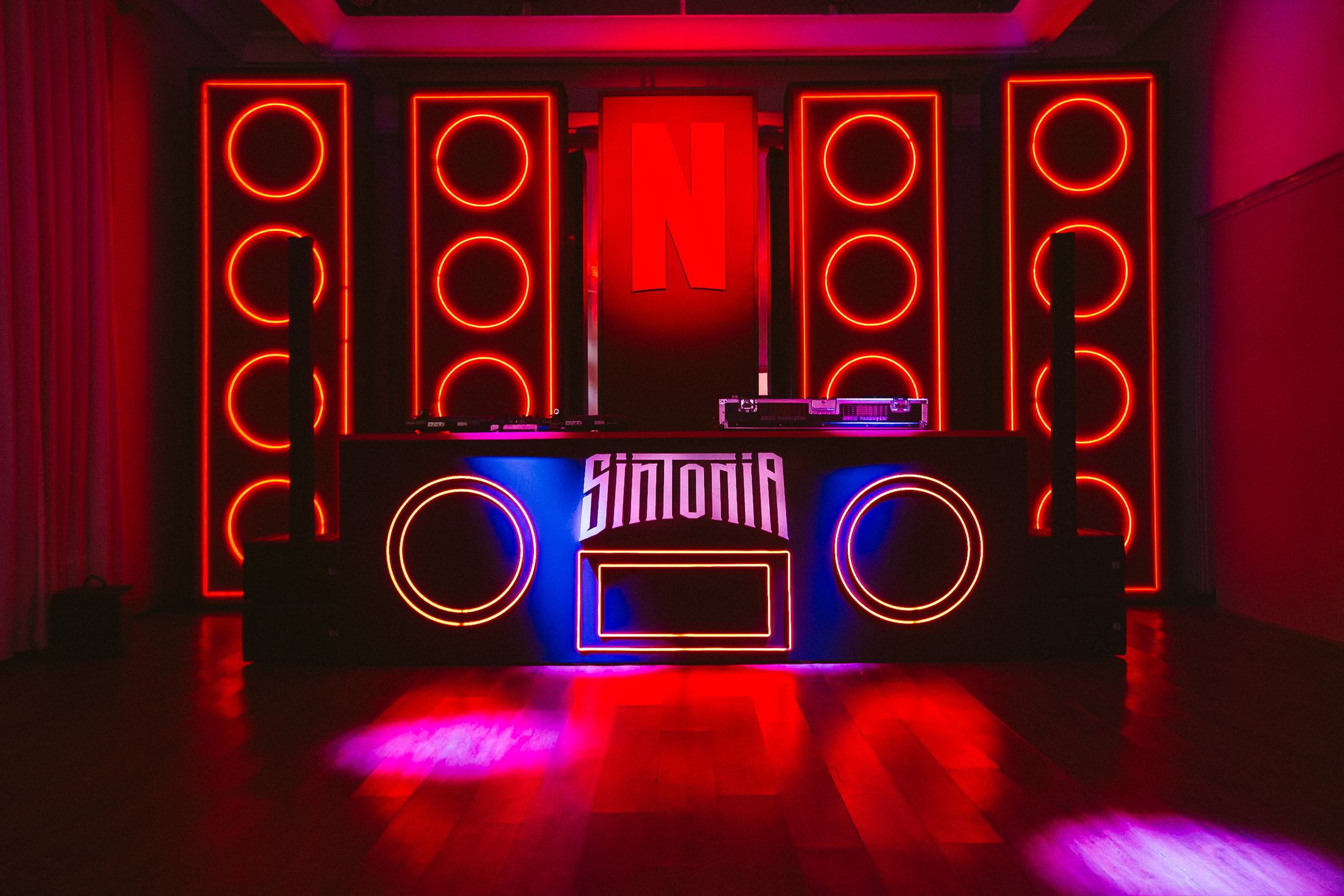 Pista Sintonia com parede de caixas de som desenhadas em neon vermelho